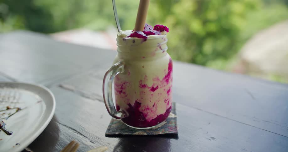 A man sets a berry milkshake down on a coaster at an outdoor table