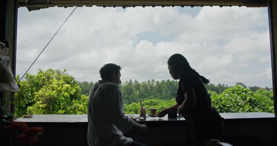 A waitress brings a cup of coffee to a man sitting on the balcony