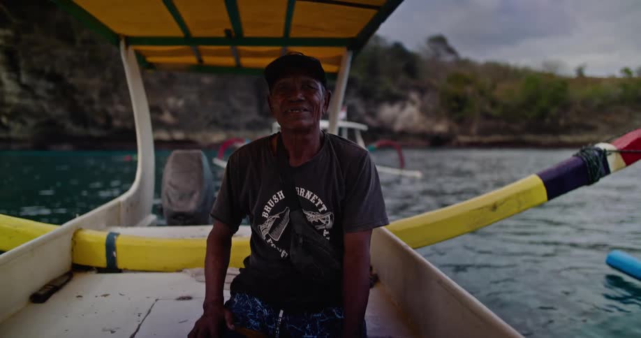 A man sitting on a small boat next to a coast line smiles at the camera