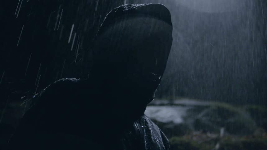 A man looks through the falling rain at the sky then walks away