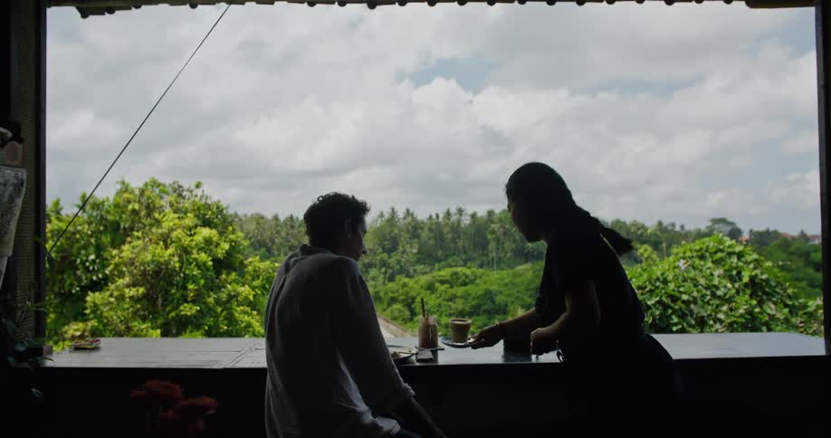 A waitress brings a man a cup of coffee on a balcony