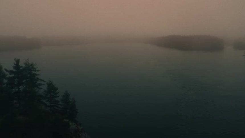 Aerial view of a river or lake surrounded by pine tree forests in the mist