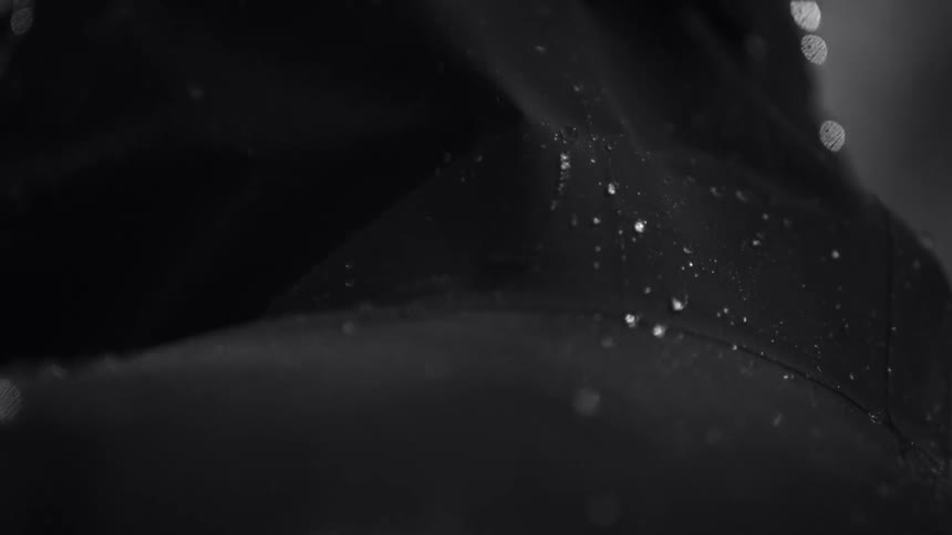 Black and white slow motion close up of water drops falling over a dimly lit silhouette