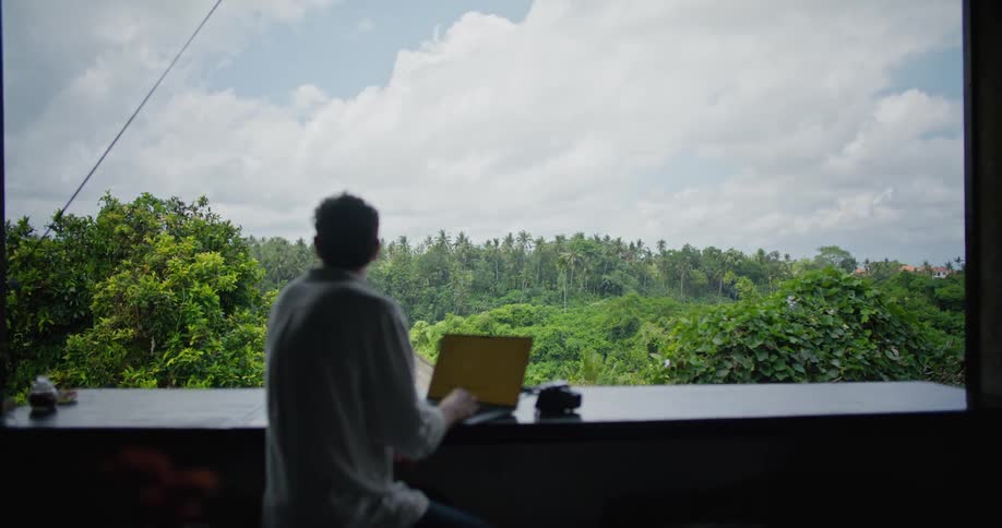Photographer sitting on the balcony of a restaurant on the tropics types on a laptop