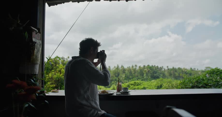 Photographer sitting on the balcony of a restaurant on the tropics takes a picture with a camera