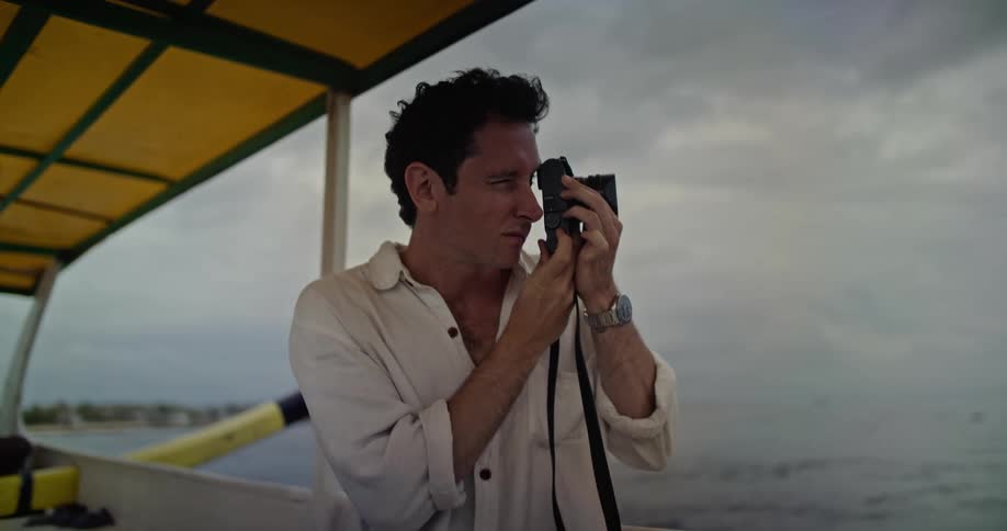Young man wearing a white shirt takes pictures while riding on a boat near the coast