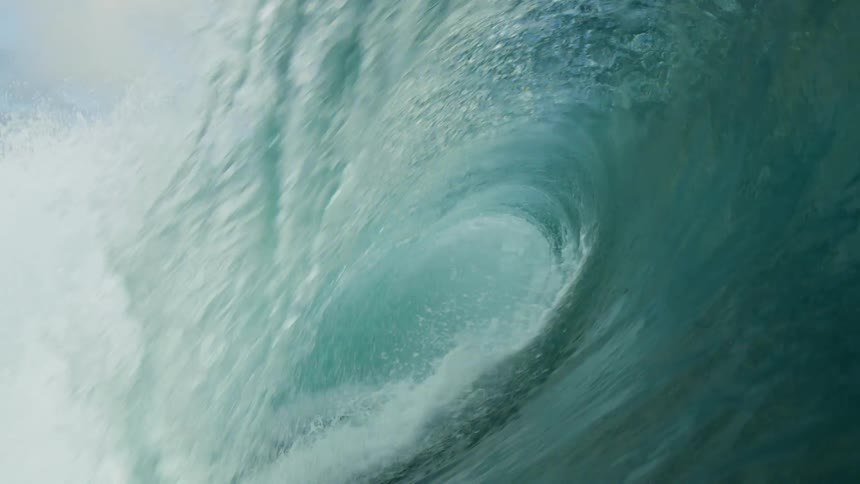 A surfer rides on top of a huge wave as it rolls in splashing overhead and then under clear blue water