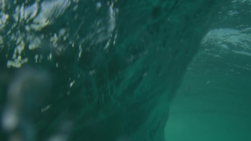 Sunlight shines on a huge wave as it rolls in splashing overhead and then under clear blue water