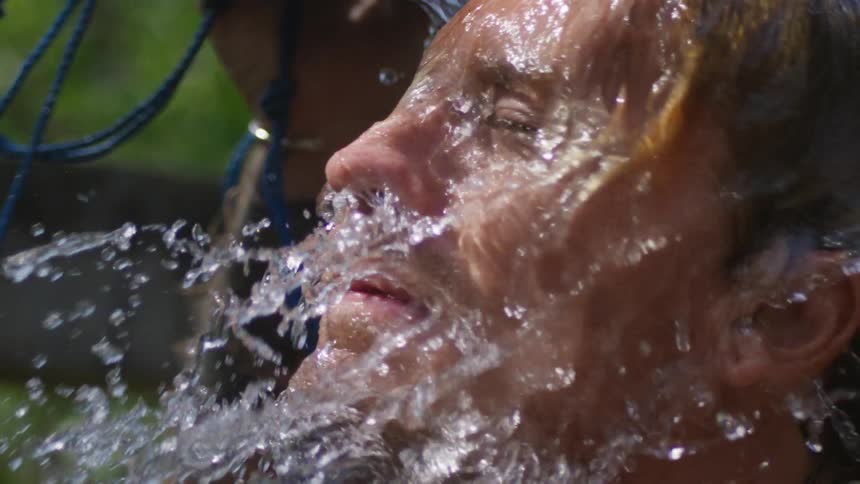 A man shakes his head back and forth while pouring water on his head