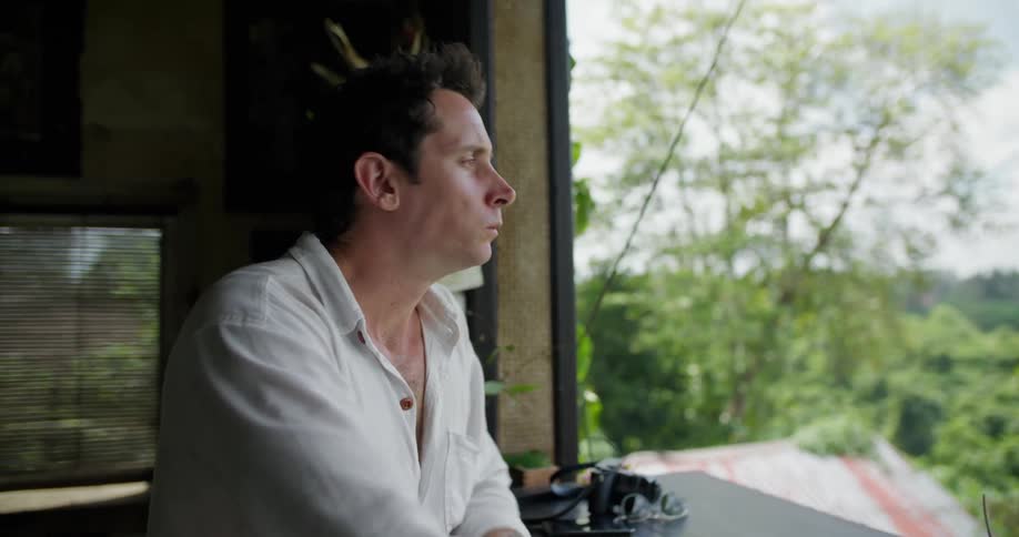 Young man sitting on a tropical restaruant balcony eating food and admiring the landscape
