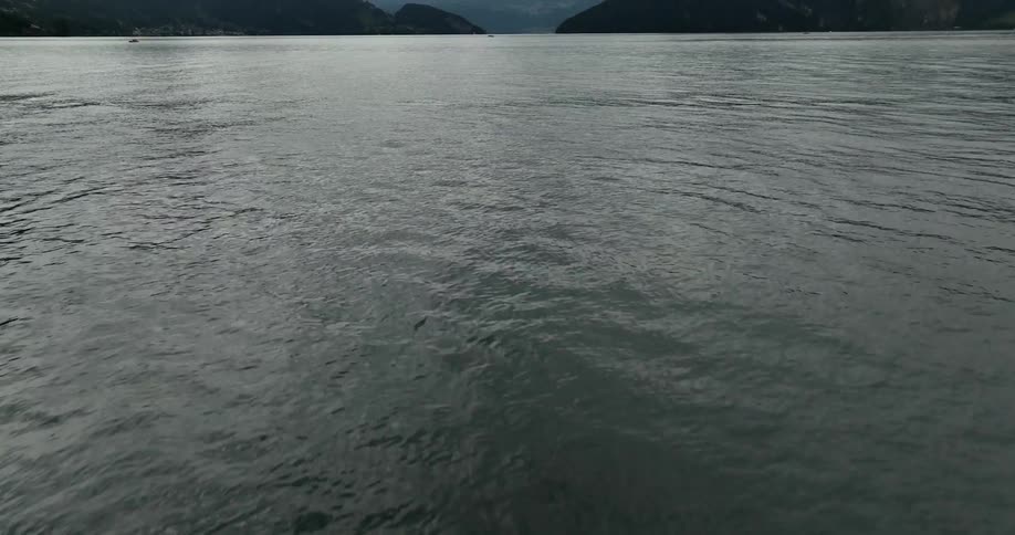 The camera points down at a body of water highly magnified then goes forward and upwards very fast to reveal a lake mountains and sky