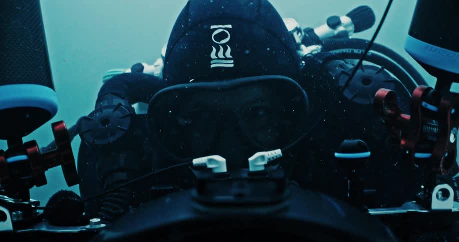 A close up of a man in scuba gear holding a camera recording underwater