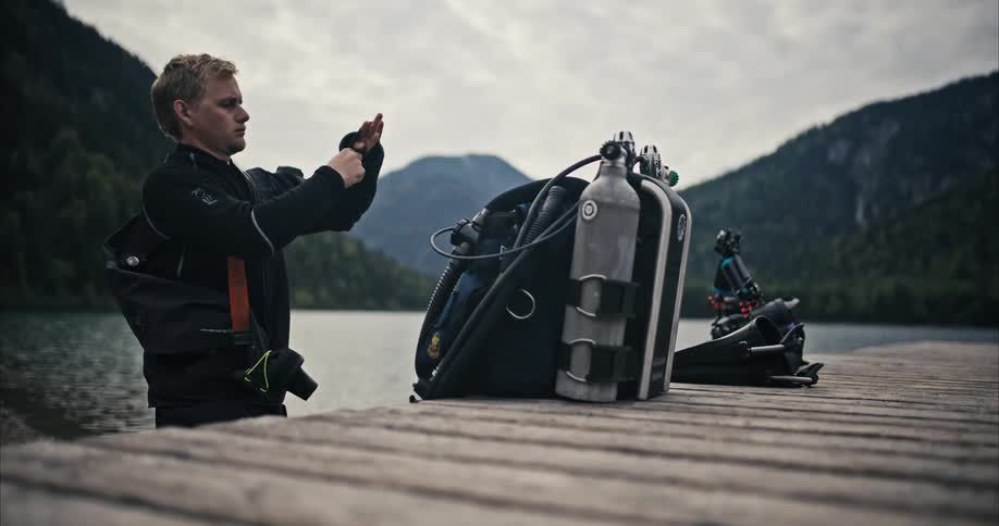 Scuba diver gearing up on a pier next to a lake in the mountains at daytime