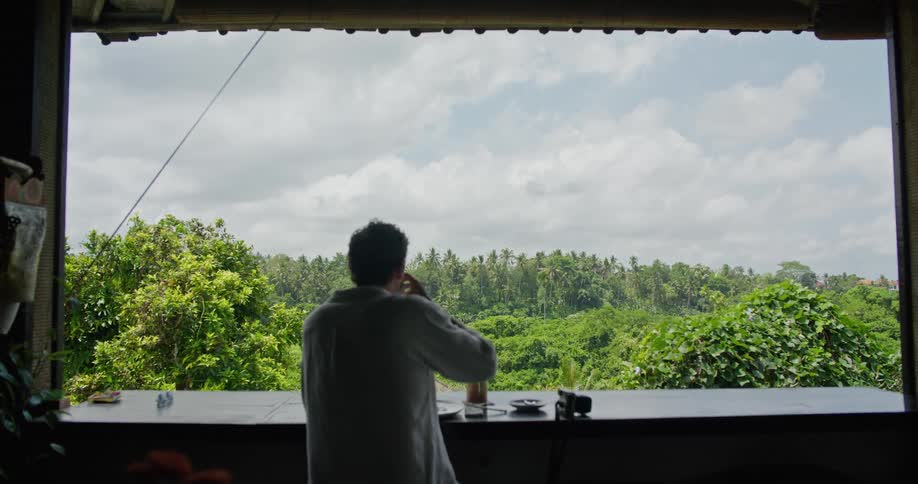 Photographer sitting on the balcony of a restaurant on the tropics takes a picture with a camera