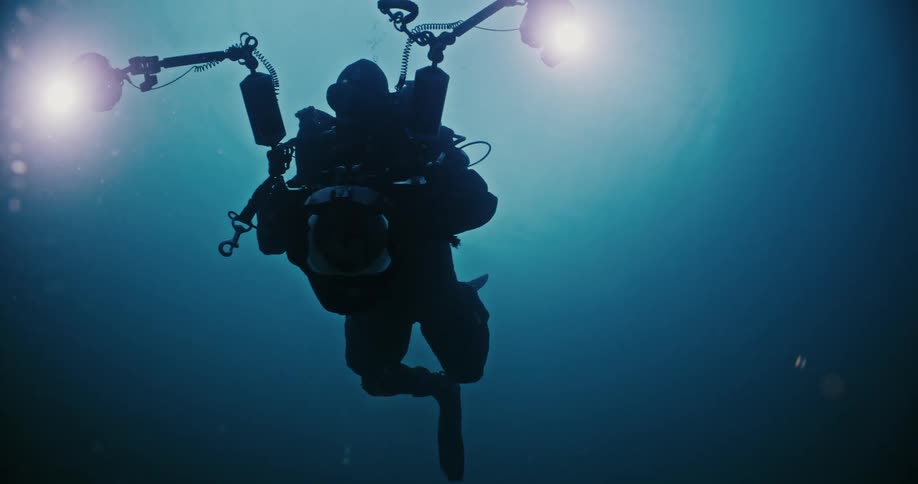 A man in full scuba diving equipment holding a camera underwater in the ocean