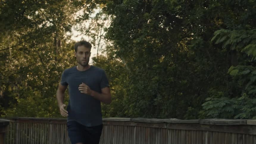 A man jogs across a wooden bridge in the evening