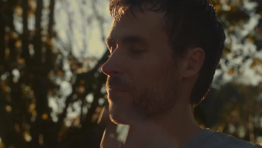 Man stands outdoors near house wiping his sweaty brow