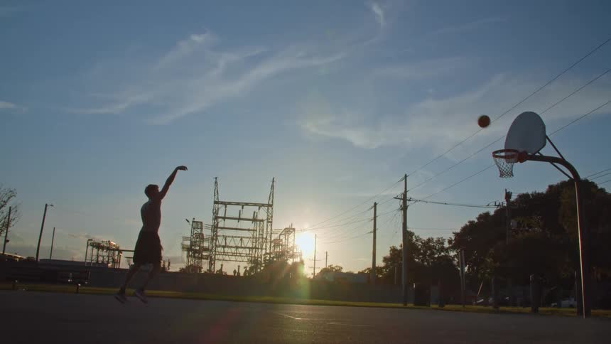 A shirtless man throws a basketball into a hoop from far away
