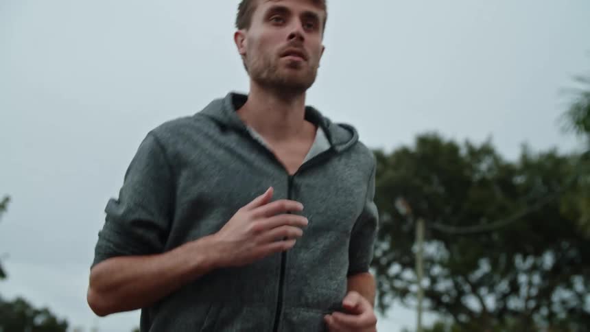 Man with gray zip up hoodie runs down the street on cloudy day