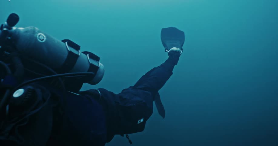 A man in scuba diving gear holding a filming camera swimming underwater in the ocean