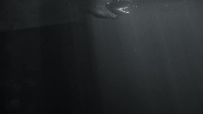 Underwater monochrome black and white footage of a persons feet dipping in the water