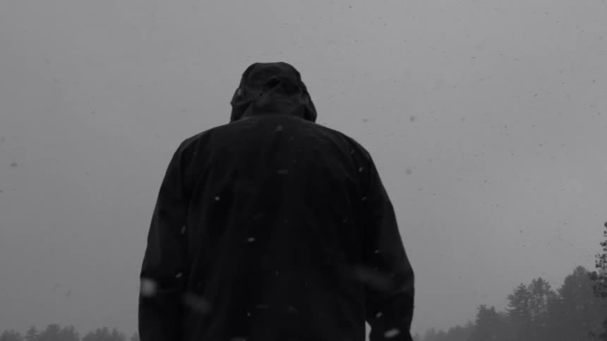 Silhouette of a man walking on a snow storm close to a pine tree forest