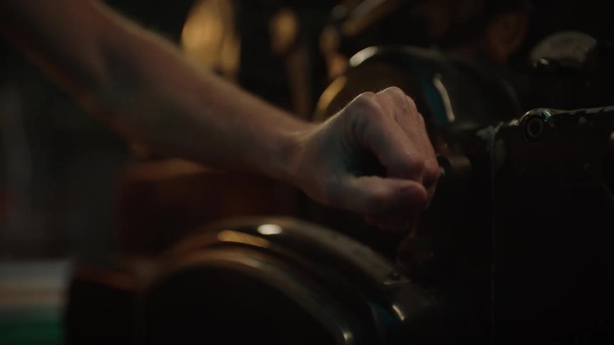 Close up of the hand of a man pushing a lever on a machine inside a workshop