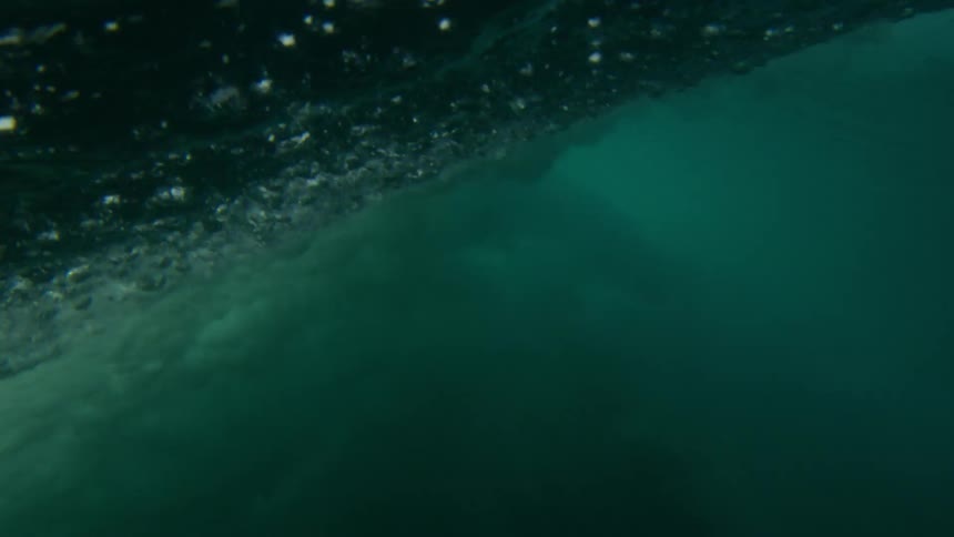 A huge wave rolls in splashing overhead and then looking up from underwater
