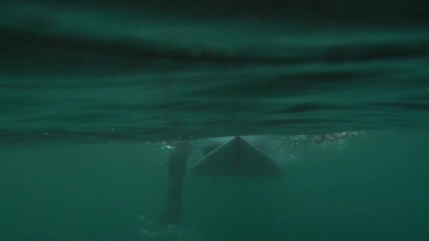 Underwater footage of a surfer paddling with his hands over a surfboard