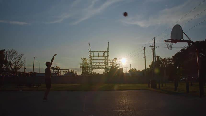 Silhouette of a young man playing basketball by himself on an outdoors court at evening