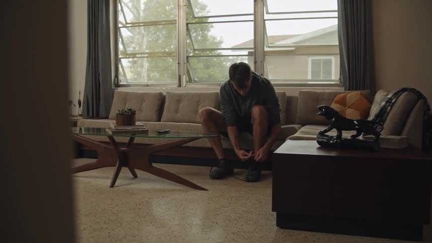 A man is sitting on a couch tying his shoelaces