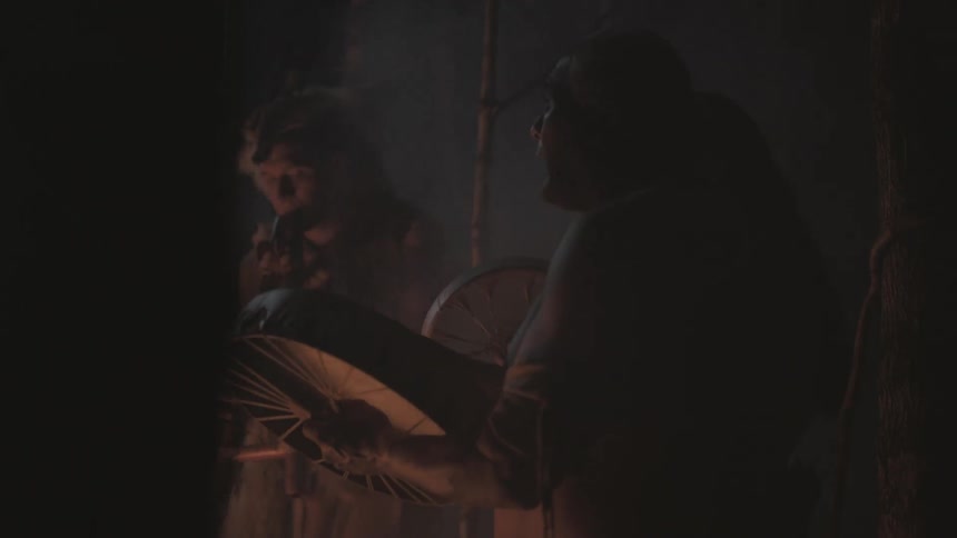 A group of native peoples are singing and playing instruments in the forest at night