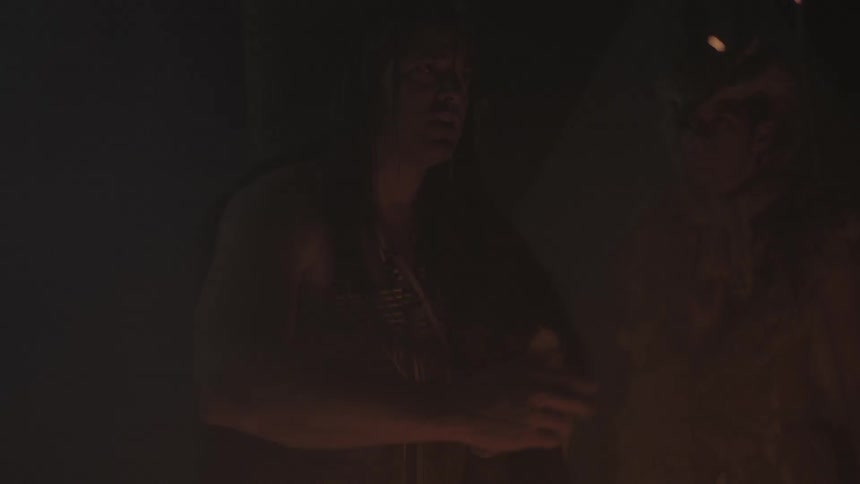A native american man stands beside a fire talking to the others