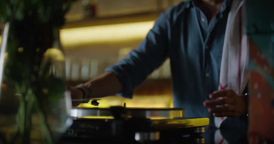 A man flips a vinyl record album in his hands as he places it on the turntable and moves the needle to play it