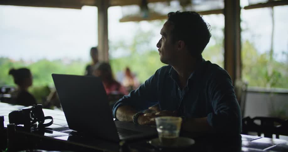 A man typing on a laptop while sitting at a restaurant bar