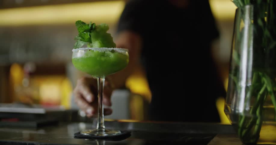 A bartender places a garnished cocktail on the bar counter