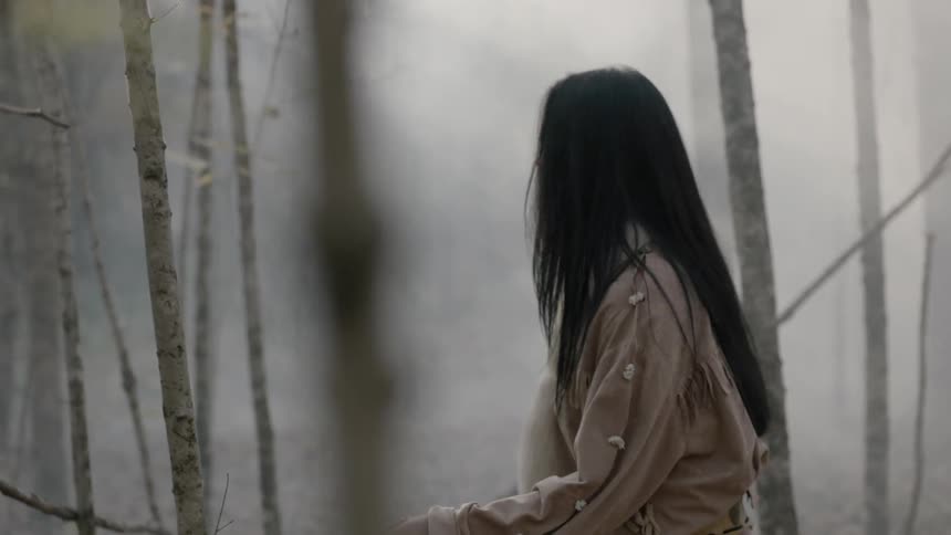 A native american woman walks through the woods