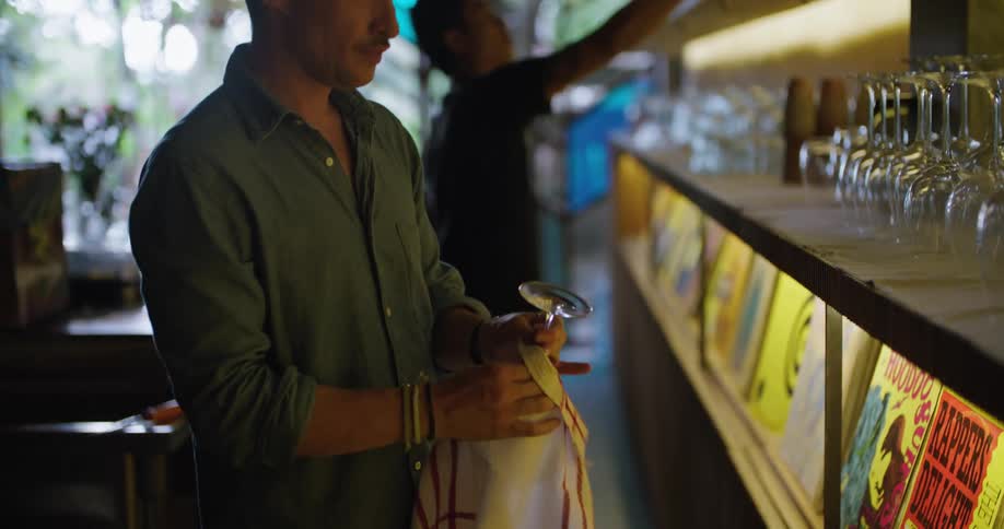 Two bartenders wipe glasses and return them to the counter