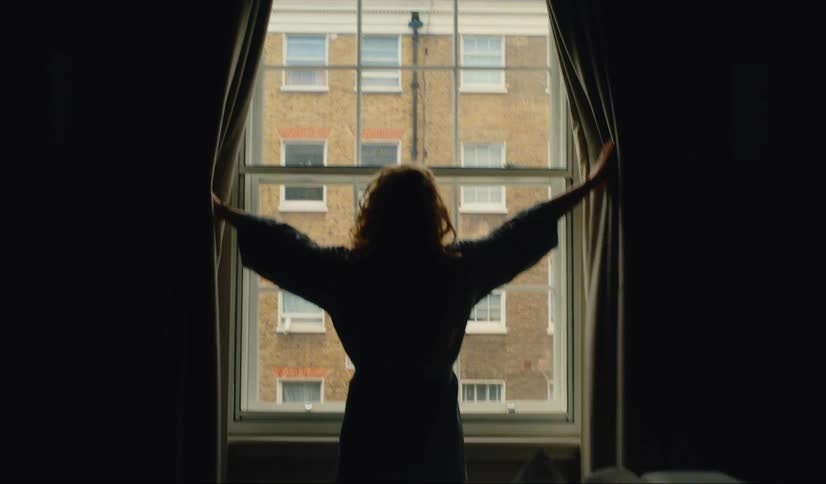 A woman opens hotel room window overlooking London street