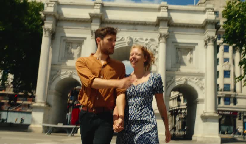 Couple walks through marble arch in London as double decker buses pass on nearby street