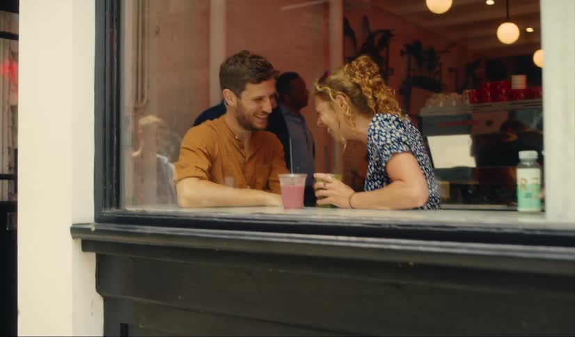 Couple laughing sat in window of coffee shop in London