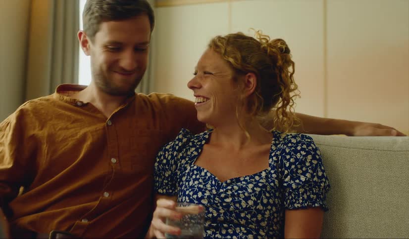 A man sits with his arm around his partner while they watch a laptop together on the couch