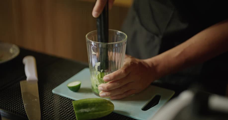 A bartender crushes lime pieces inside a glass with a muddler as he stands behind the bar