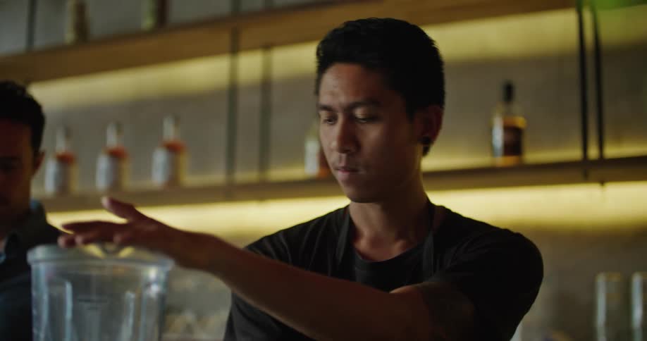 Bartender preparing a drink with a blender at the bar counter with a coworker next to him