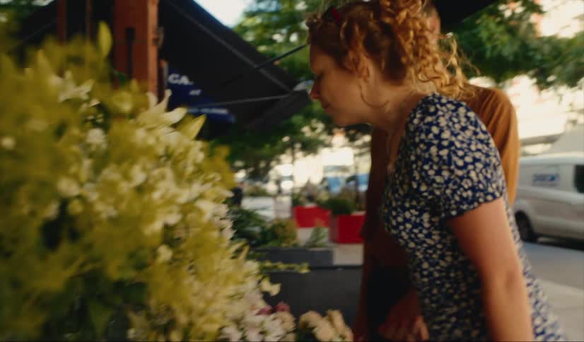 A woman with a man on a street stops and smells some flowers outside of a shop in Mayfair, London