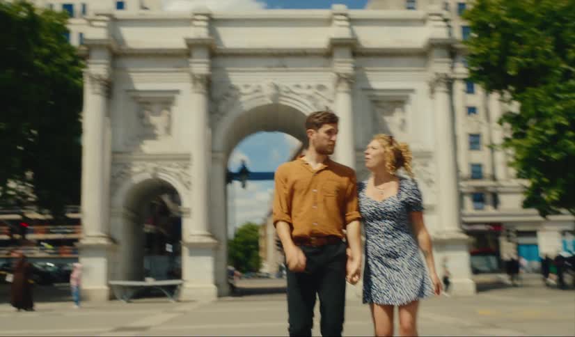 A couple hold hands while walking through marble arch in london