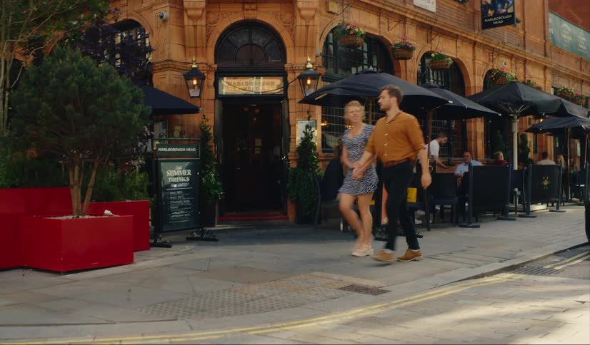 A man and a woman hold hands as they walk past a pub in Mayfair, London
