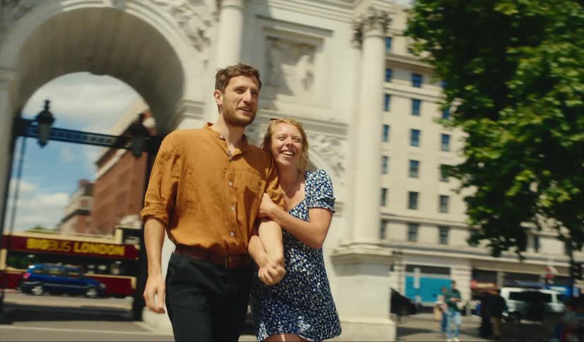 A man and a woman are holding hands and talking as they walk through Marble Arch