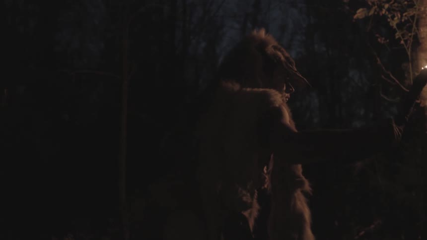 Person walking through a dimly lit area with only the light of a candle