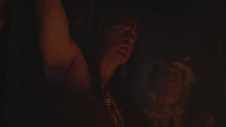 A native american woman speaks to those around campfire